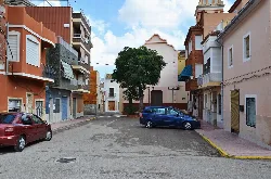 Square with trees, residential buildings, and two parked cars.