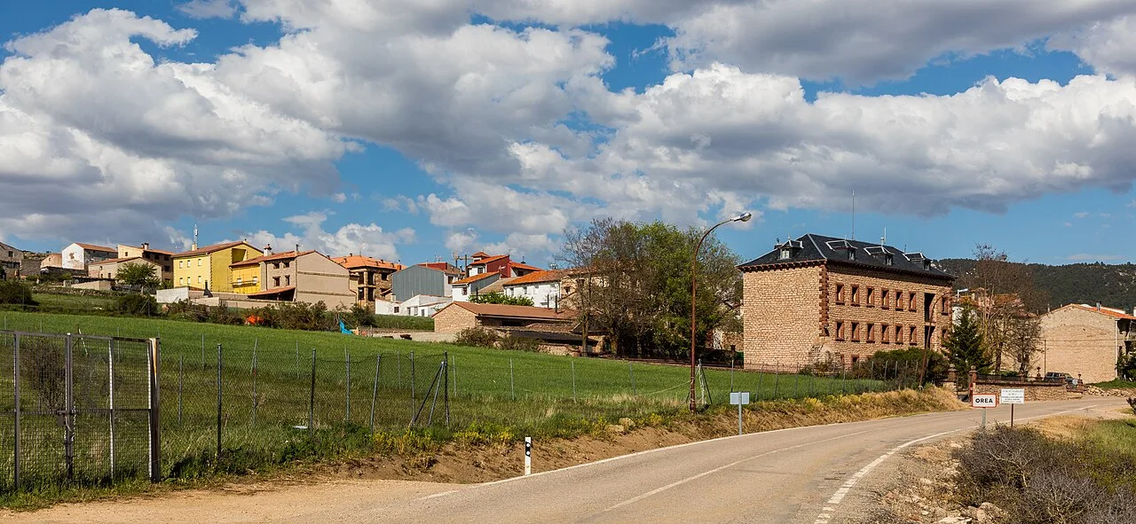 Bunte Häuser und ein großes Gebäude in Orea, Guadalajara, mit bewölktem Himmel.