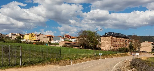 Bunte Häuser und ein großes Gebäude in Orea, Guadalajara, mit bewölktem Himmel.