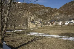 Kirche Sant Feliu und Häuser in Barruera, Valle de Bohí, mit Bergen im Hintergrund.