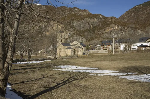 Kirche Sant Feliu und Häuser in Barruera, Valle de Bohí, mit Bergen im Hintergrund.