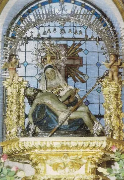 Statue of the Virgin of Piety with Jesus, surrounded by golden angels and a stained glass window in the background.