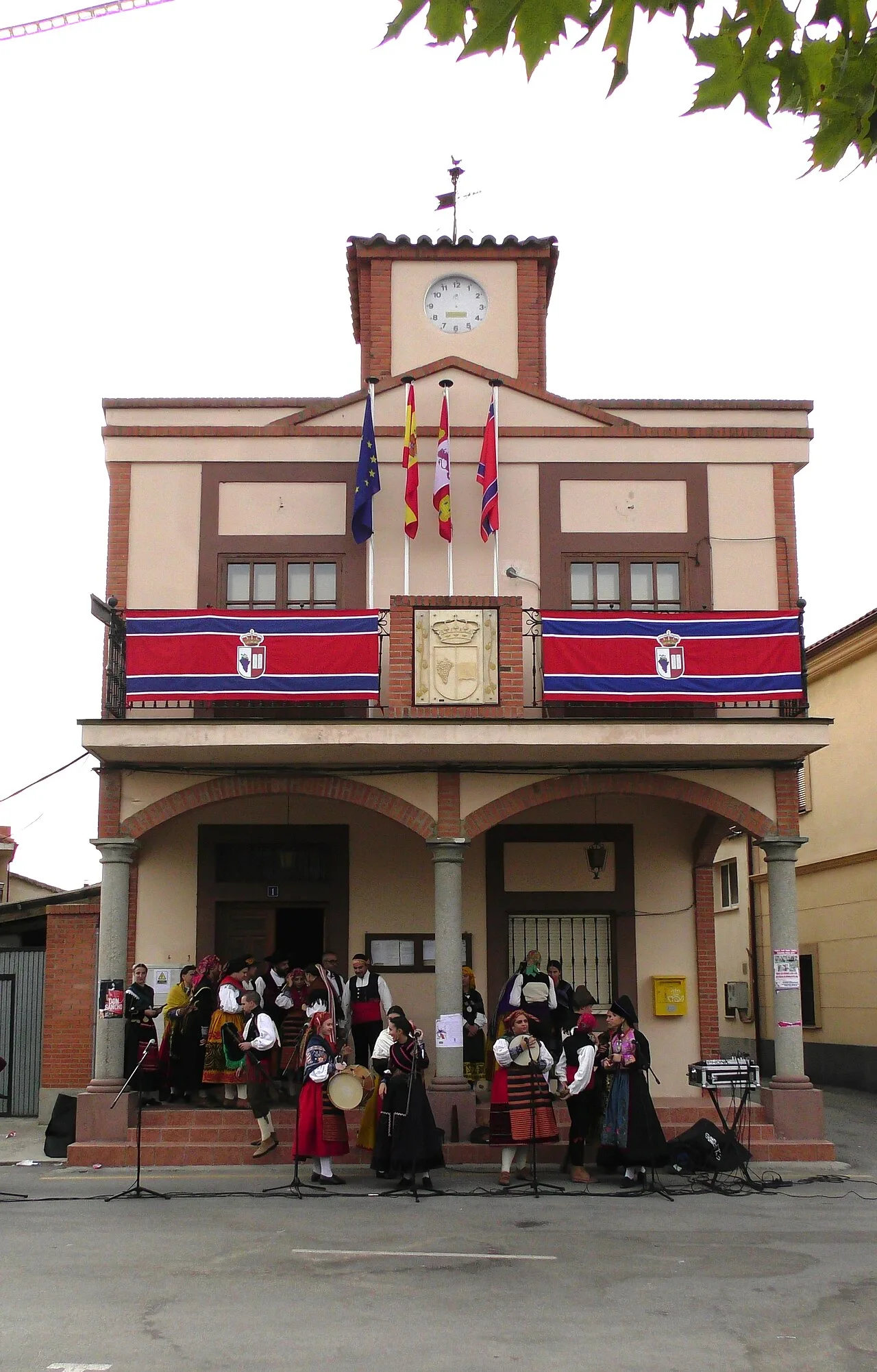 Town hall building with flags and people in traditional costumes at the entrance.