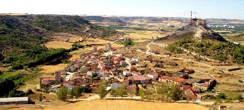 Vista aérea de un pueblo con castillo y colinas verdes.