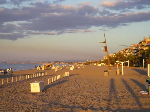 Playa con arena dorada, sombrillas apiladas y edificios junto al mar al atardecer