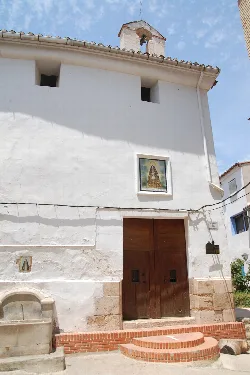 Weiße Kirchenfassade mit Holztür und kleinem Glockenturm in Chelva.