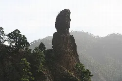 Large rock formation in a mountainous landscape with trees and fog.
