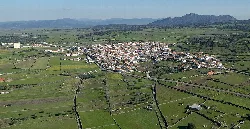 Vista aérea de un pueblo con campos verdes y montañas al fondo.