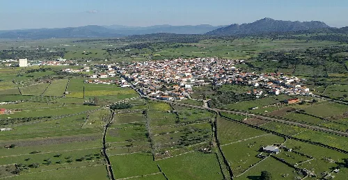 Luftaufnahme eines Dorfes mit grünen Feldern und Bergen im Hintergrund.
