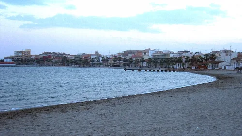 Strand mit Schatten und Stadt im Hintergrund.