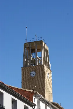 Kirchturm in Buñuel mit Uhr und Struktur vor blauem Himmel.