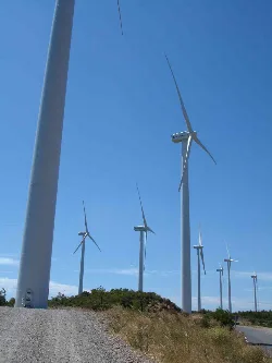Mehrere Windturbinen auf einem Hügel unter einem blauen Himmel.