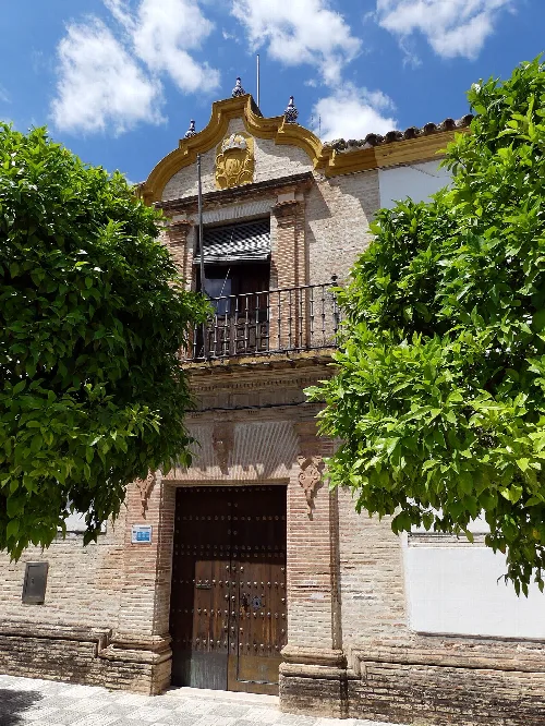 Facade of an old house with wooden doors and iron balconies, surrounded by green trees.