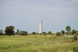 Torreta de agua en Saucedilla rodeada de árboles y campo verde.