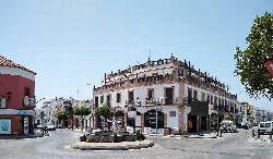 Roundabout with monument in the center, surrounded by buildings and trees.