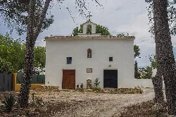 Weiße Kapelle mit Holztüren und kleinem Altar im Freien in Benigánim.