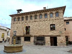 Stone building with flags and a fountain in the square.