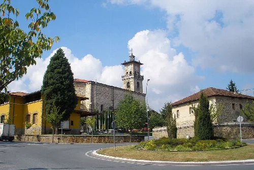 Kirche und Häuser in Amurrio mit Bäumen und wolkigem Himmel.