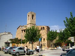 Old church with tower in Cunit, Tarragona, in a square with trees and people.