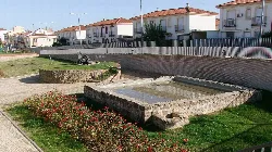 Rectangular stone water fountain with water, surrounded by grass and flowers in Bailén.