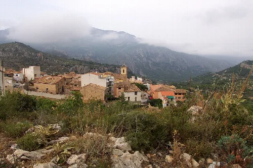 View of houses in Confrides with mountains and clouds in the background.