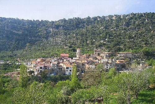 Panoramablick auf ein Dorf auf einem Hügel mit Vegetation und Bergen im Hintergrund.