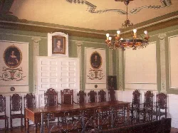 Room with long table, chairs, and paintings on the walls.