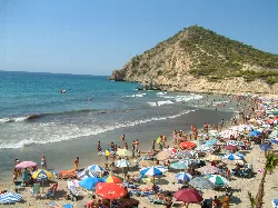 Strand mit Sonnenschirmen, Schwimmern und einem grünen Hügel in Finestrat.