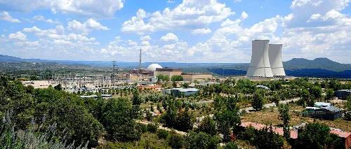 Nuclear power plant with cooling towers and dome in a green landscape.