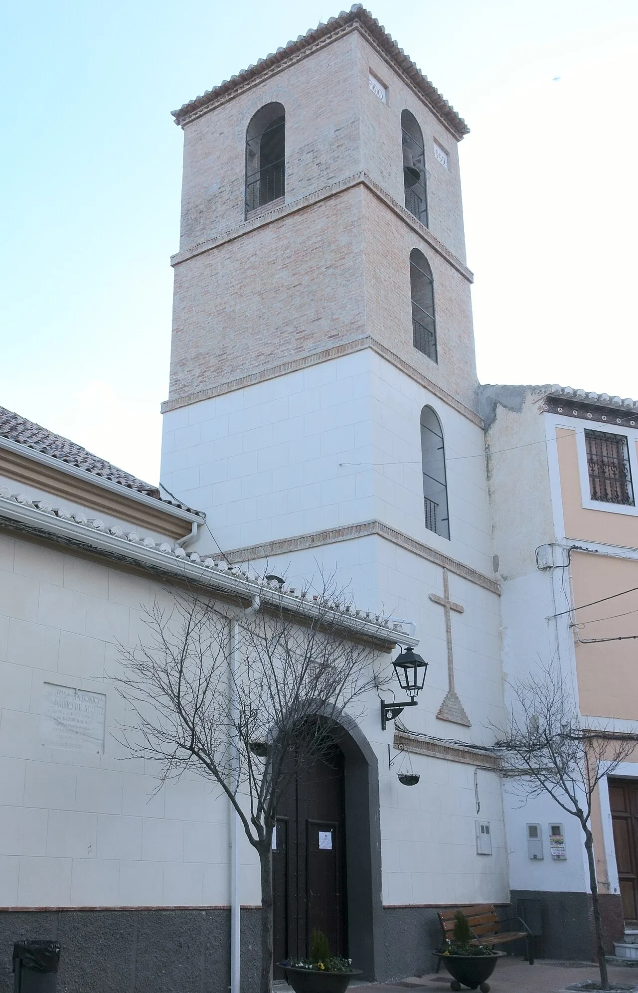 Torre de la iglesia con ventanas arqueadas y una cruz en la fachada.