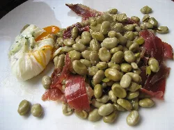 Fava beans with ham and egg flower on a plate, with a poached egg on the side.