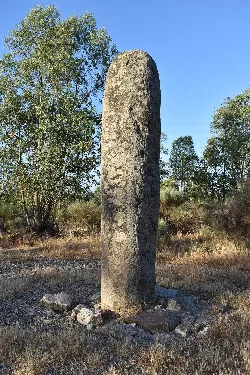 Menhir de Cabezo in einer natürlichen Landschaft mit Bäumen und trockenem Gras.