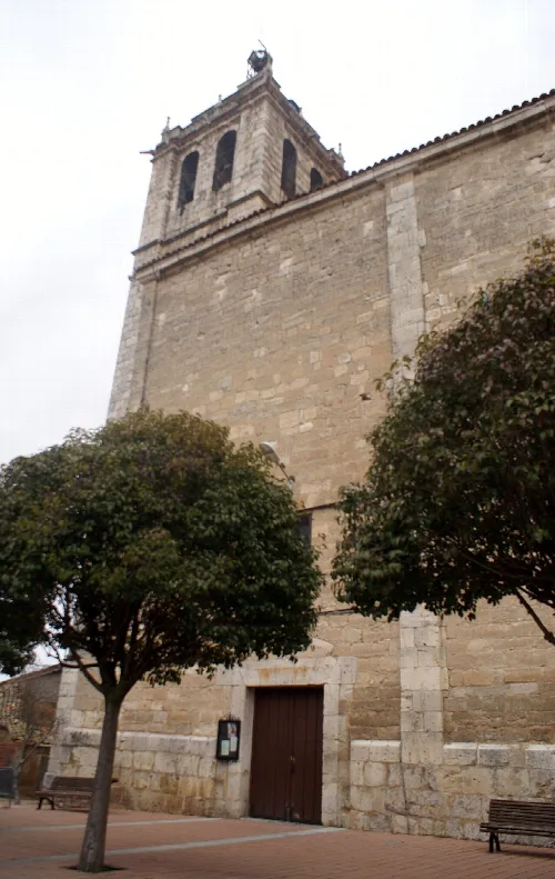 Torre de piedra de la iglesia de Cabezón de Pisuerga con árboles en primer plano.