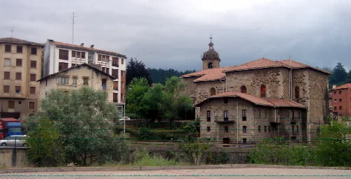 Iglesia antigua en Igorre con edificios modernos y árboles.