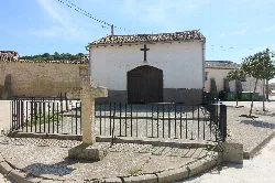 Pequeña capilla blanca con cruz y verja de metal en Valverde de Campos.