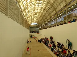 Interior of a trinquet with spectators and players on the court.