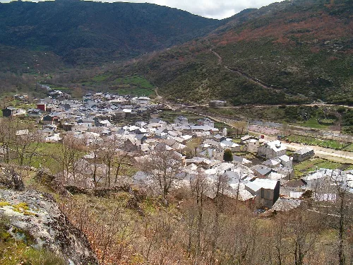 Ein Dorf mit Häusern und Bergen rundherum von einem Hügel aus