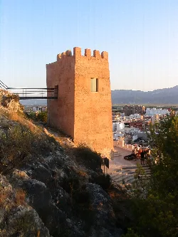 Torre de color terracota en una colina con vista a Cullera y montañas.