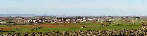 Panorámica de un pueblo con campos y montañas al fondo.