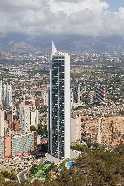 Tall skyscraper in Benidorm with mountains and city behind.