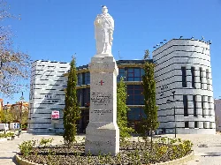 Teatro y monumento en una plaza de Valdepeñas, con árboles y un cielo azul.