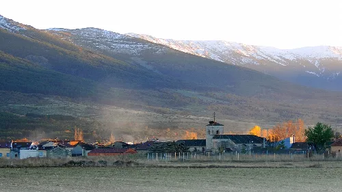 Landschaft mit Dorf und schneebedeckten Bergen im Hintergrund.