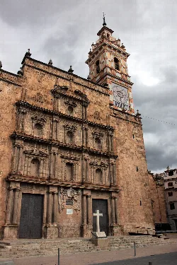 Fachada de piedra de la iglesia con torre y reloj en Chelva.