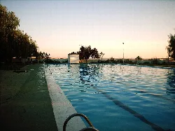 Piscina pública con agua azul y árboles alrededor, al atardecer.