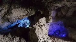 Interior de una mina con rocas y luces azules y moradas.