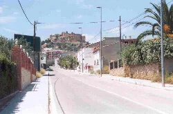 Calle en Montesa con casas y un castillo en la colina al fondo.