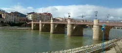 Puente de piedra con arcos sobre el río Ebro, con edificios y farolas en el fondo.