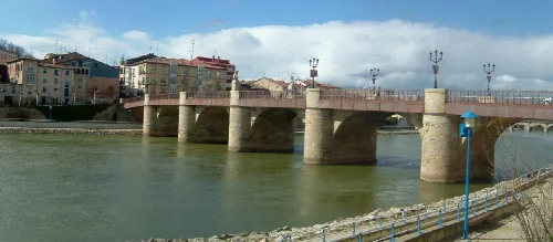 Stone bridge with arches over the Ebro River, with buildings and lampposts in the background.