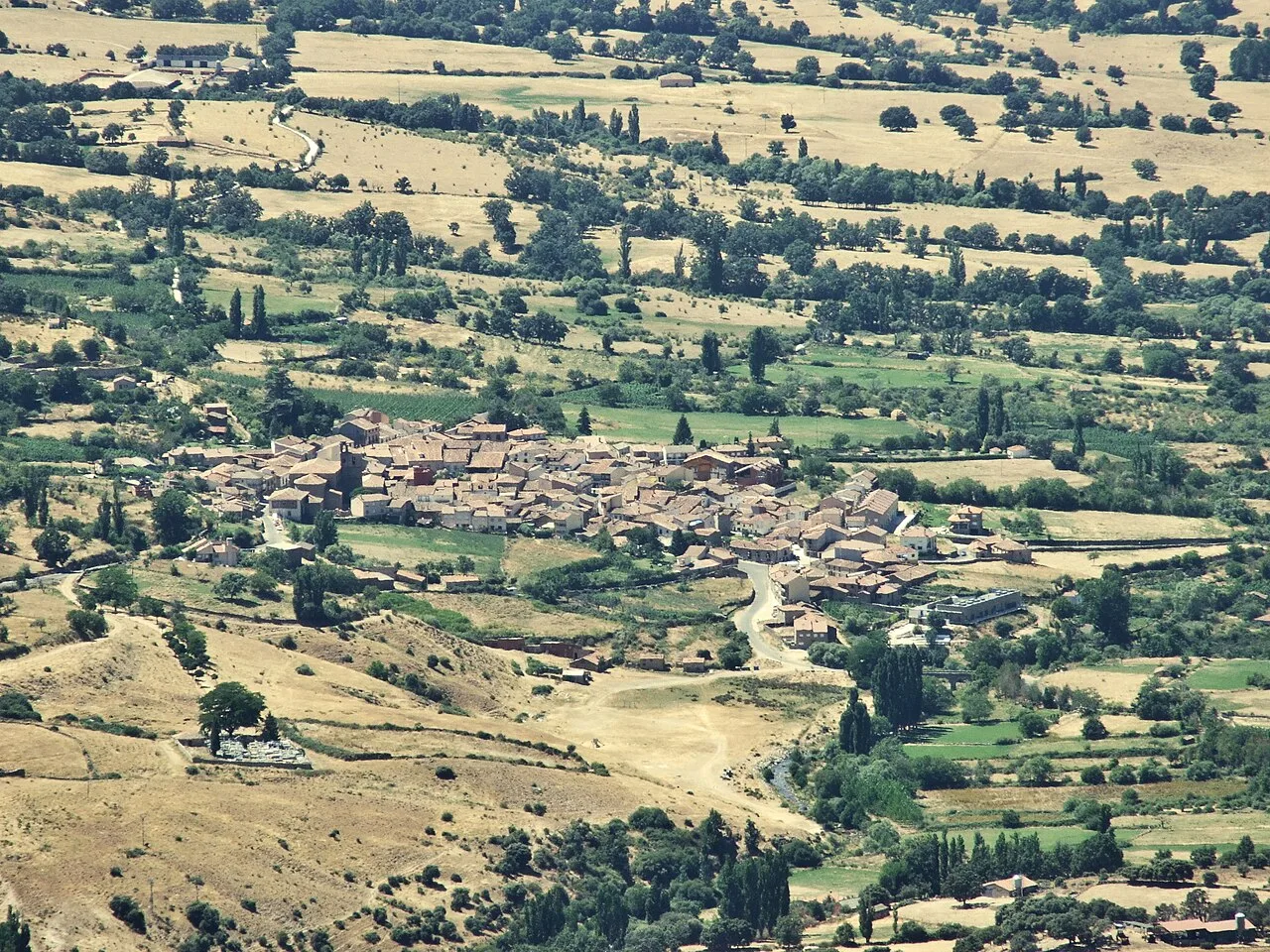 View of a village surrounded by fields and hills from above.