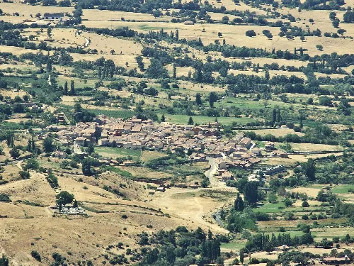 Blick auf ein Dorf umgeben von Feldern und Hügeln von oben.